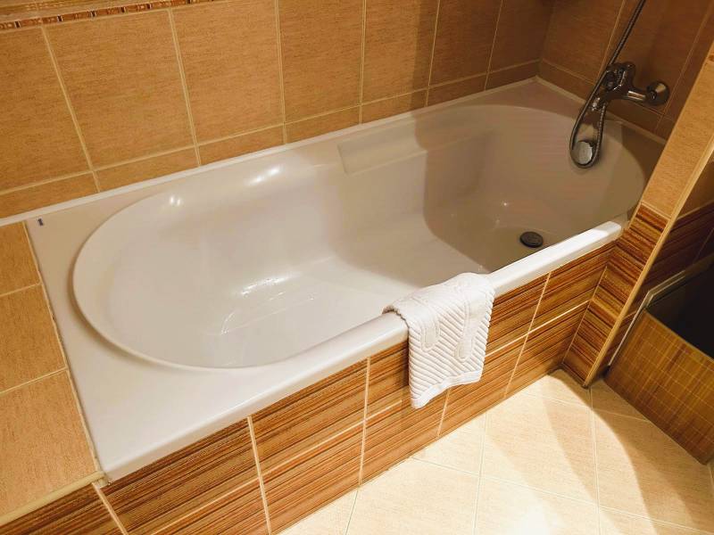 A bathroom in a studio apartment with a bathtub and ochre tiles.