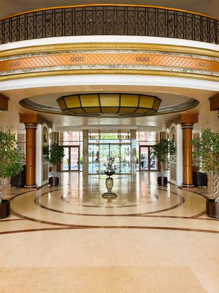 Hotel lobby with marble flooring, high ceiling, and decorative lighting.