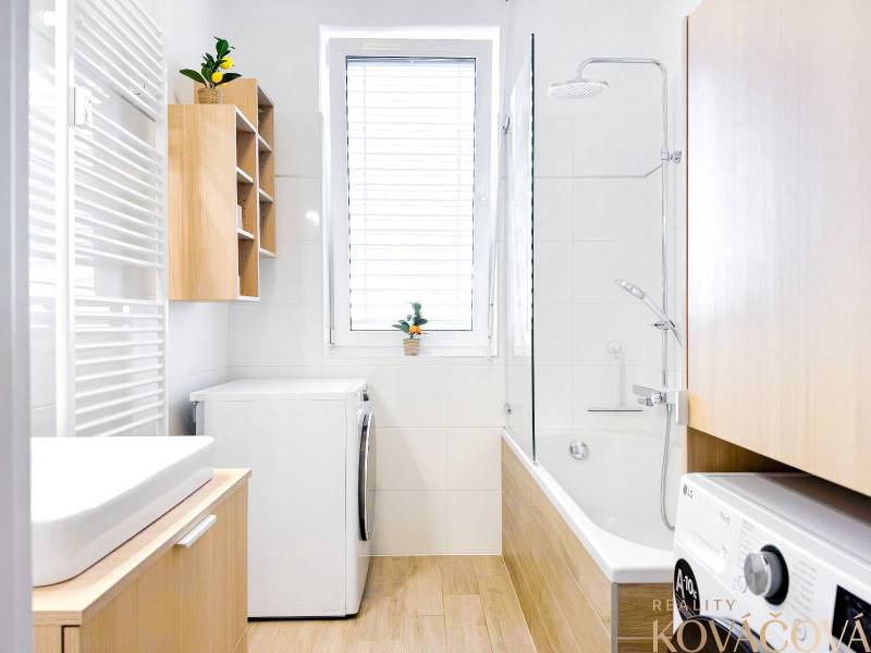 Bathroom in a 3-room apartment with a bathtub, washing machine, and floor with wooden decor.