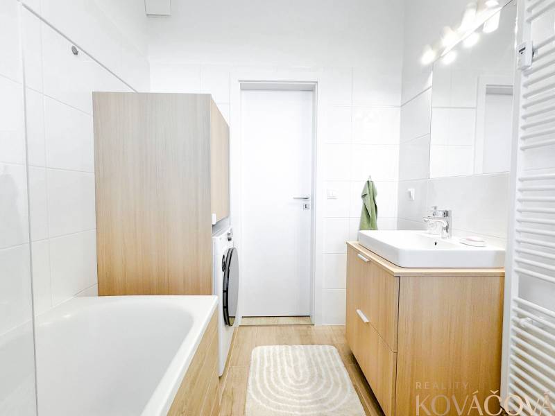 A bathroom with a bathtub, sink, and washing machine in a 3-room apartment with a wooden decor floor.