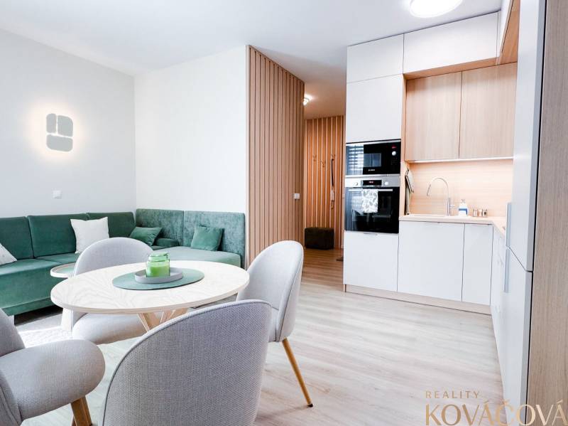 Living room and kitchen in a 3-room apartment with a wooden decor floor and a green sofa.
