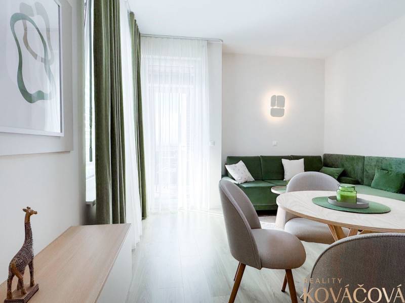 A living room with a wooden decor floor, a green sofa, and a dining table in a 3-room apartment.