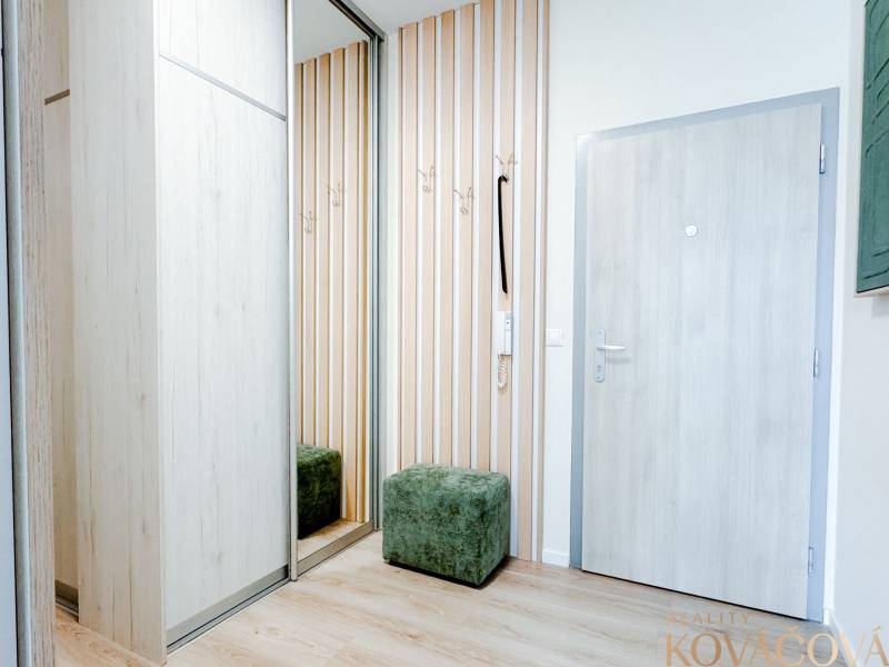 A hallway in a 3-room apartment with a wooden decor floor, coat racks, and a mirrored wardrobe.