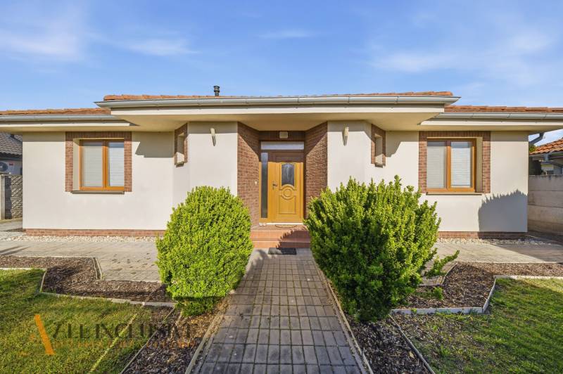 A family house in Kútniky with shrubbery, a white facade, and brown accents.