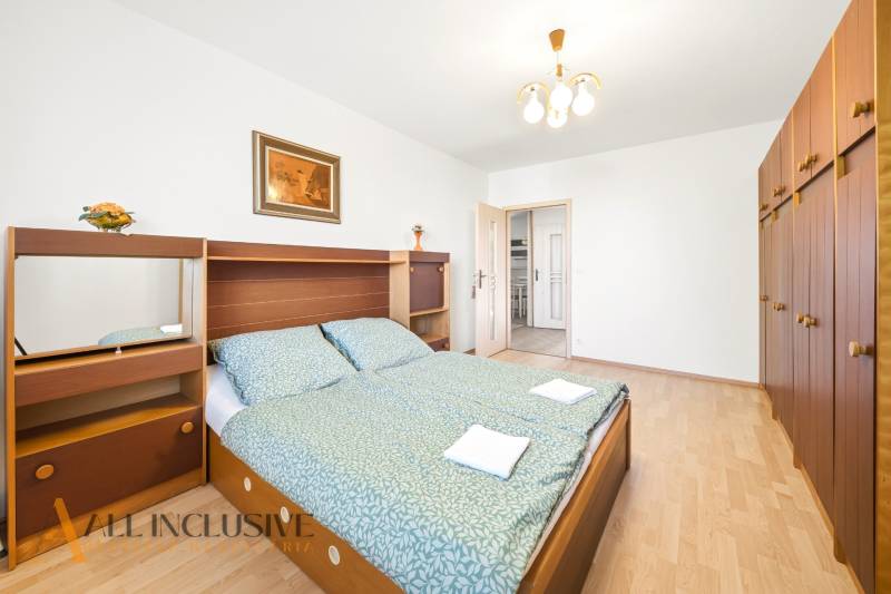 A bedroom in a family house with a large bed, a wardrobe, and a floor with a wooden decor.