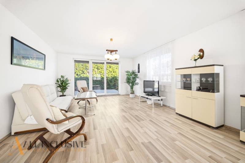 A bright living room with wood-patterned flooring, a sofa, an armchair, and a television.