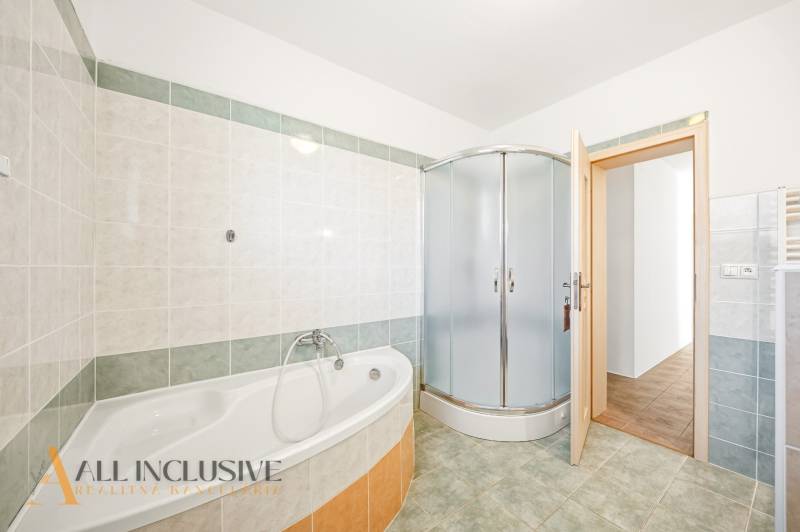 A bathroom in a family house with a bathtub, a shower corner, and tiled walls.