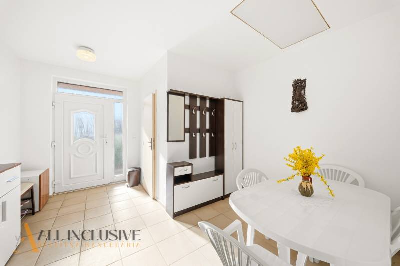The interior of a family house with a white table, plastic chairs, and a coat rack wall.