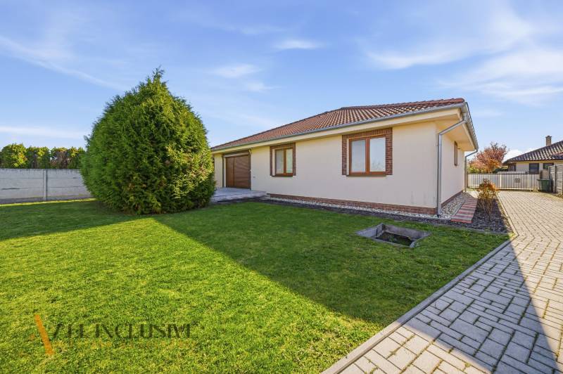 A family house in Kútniky with a lawn, trees, and paving.