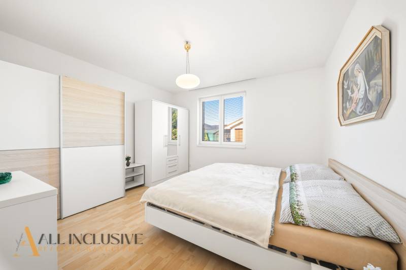 A bedroom in a family house with a wooden decor floor, white furniture, and a painting.