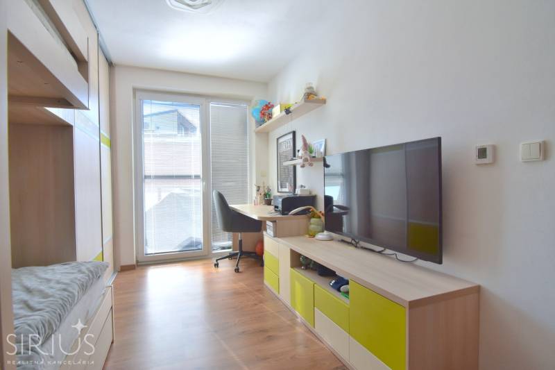 A room with a wooden floor, a desk, and a television in a three-room apartment.