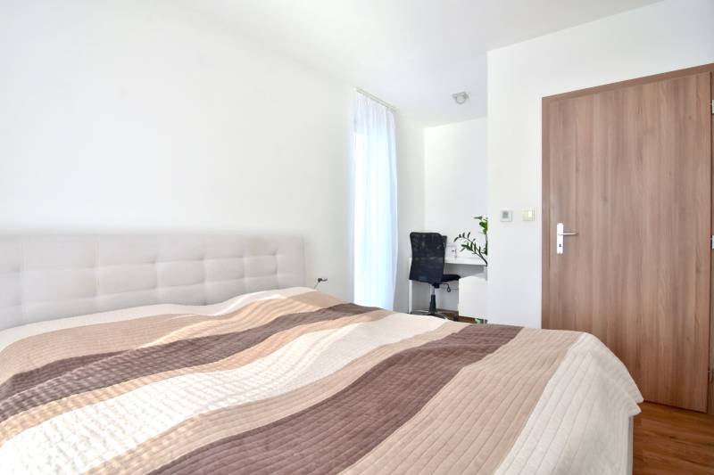 A bright bedroom with a bed, a desk, and a wooden decor floor in a three-room apartment.