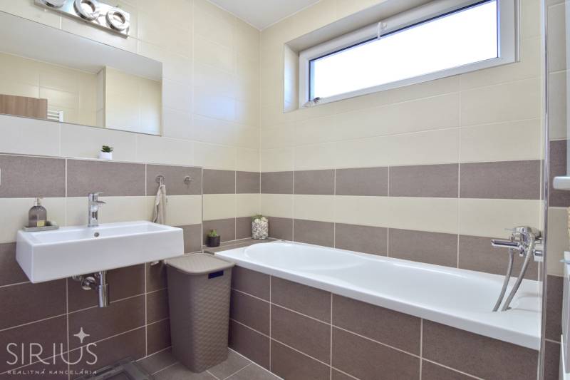 A bathroom with a bathtub and a sink in a 3-room apartment with beige tiles.