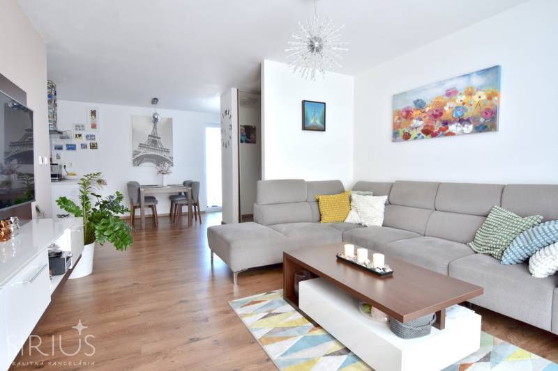 Living room in a 3-room apartment with a sofa, decorations, and a wooden-patterned floor.