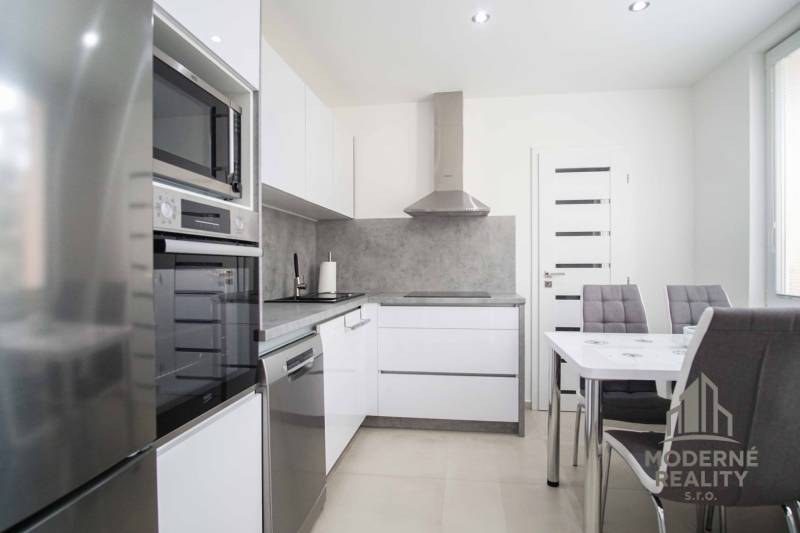 A kitchen in a 2-room apartment with glossy appliances, gray walls, and a dining table.