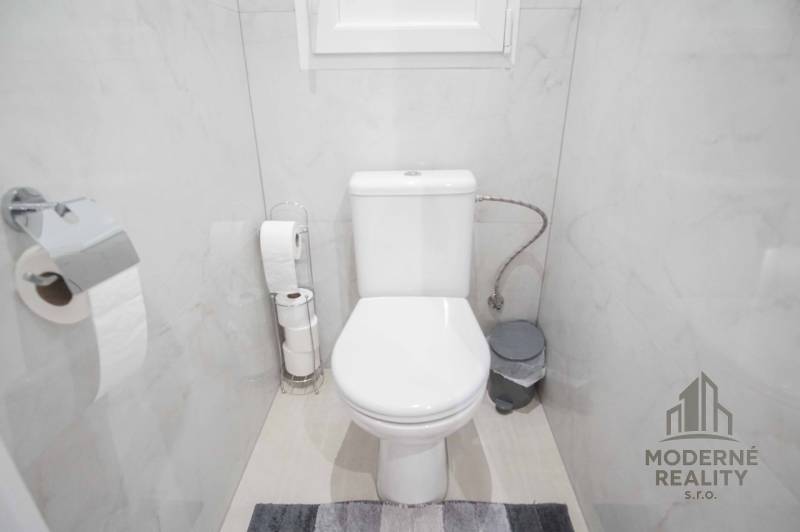 Bathroom with toilet in a 2-room apartment, light tiles and accessories in neutral colors.