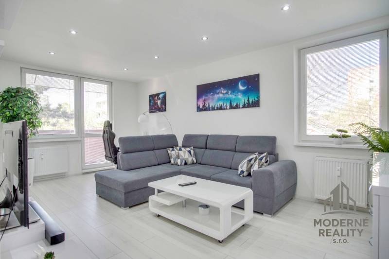A bright living room with a sofa and wood-patterned flooring in a two-room apartment.