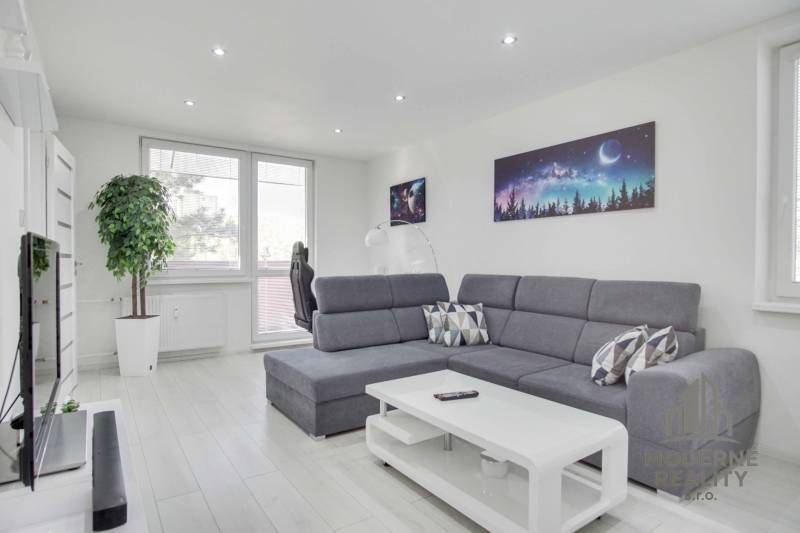 A bright living room with a corner sofa, space-themed decor, and a wood-patterned floor.
