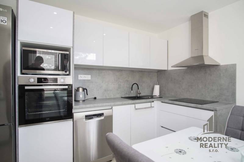 A modern kitchen with white cabinets in a 2-room apartment, equipped with appliances and a range hood.