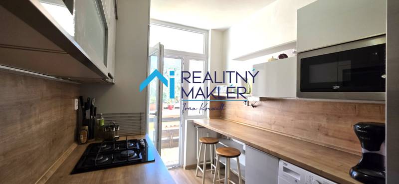 A kitchen in a 3-room apartment with a bar counter, microwave, and cooktop.