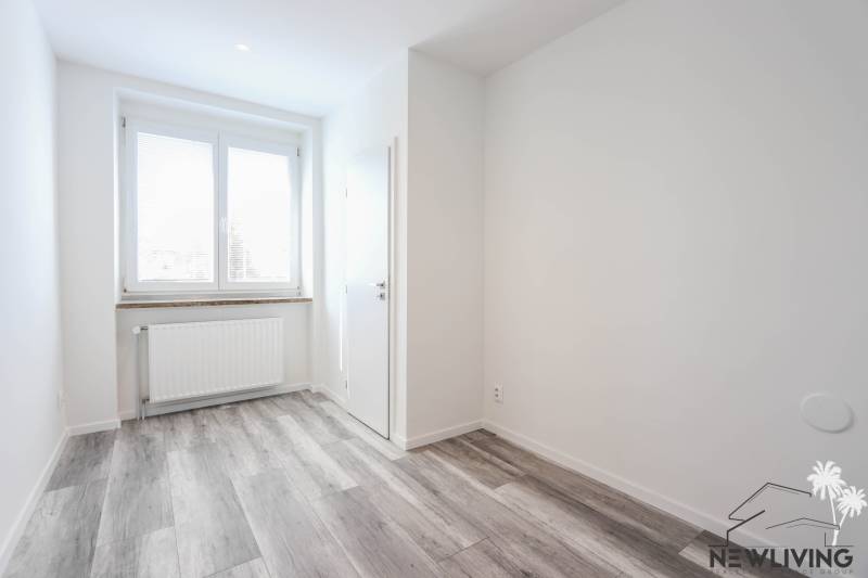 A bright room with wood-patterned flooring and a window in a three-room apartment.