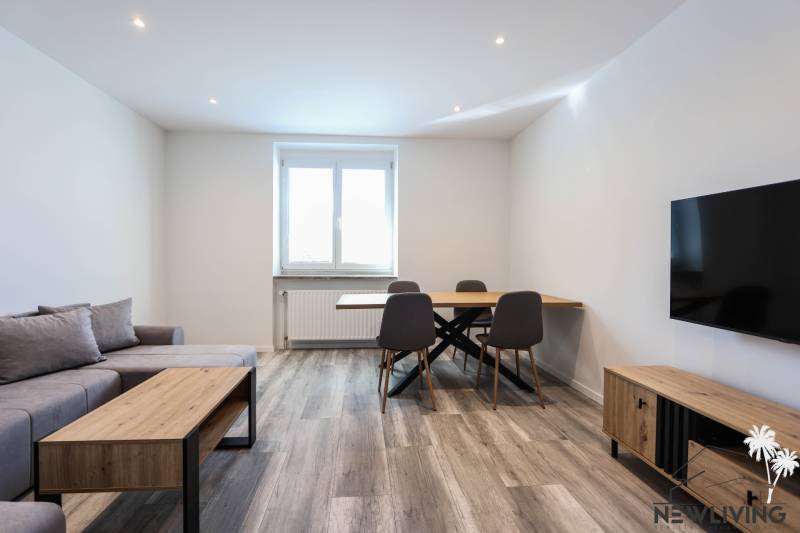 Living room with wood-patterned flooring, a sofa, a dining table, and a television in a 3-room apartment.