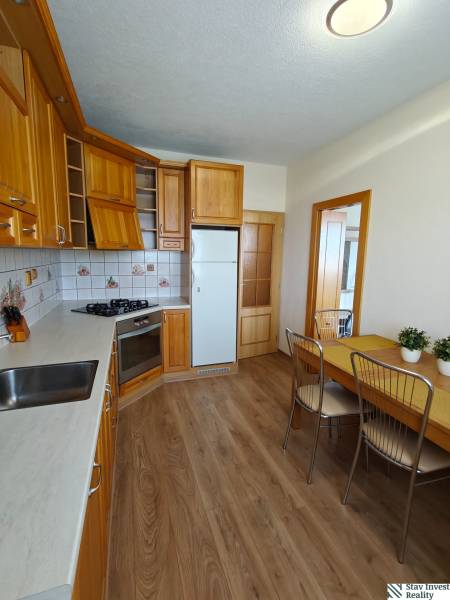 A kitchen in a 3-room apartment with a wooden decor floor and a corner kitchen unit.