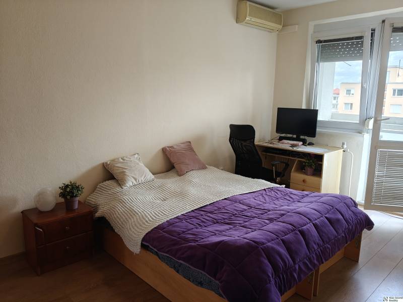Bedroom in a 3-room apartment with a bed, a work corner, and a wooden decor floor.