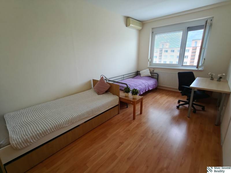 A room in a 3-room apartment with two beds, a work desk, and a floor with a wooden decor.