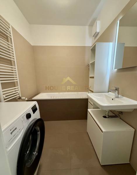 A bathroom with a washing machine and a bathtub in a 2-room apartment, neutral color tones.