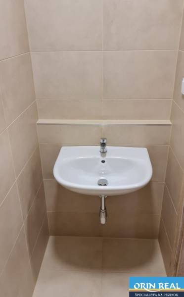 A sink in the bathroom of a studio apartment with tiles in neutral tones.