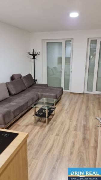 A studio apartment with a comfortable sofa, a glass table, and a floor with a wooden decor.