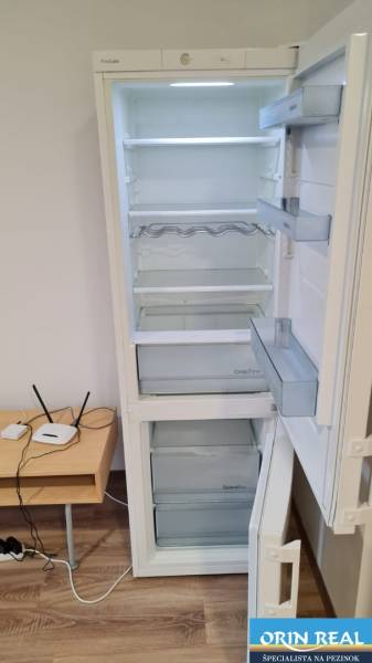 A refrigerator opening in a studio apartment with a wooden floor and a small table.