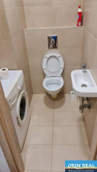 A bathroom in a studio apartment with a toilet, washing machine, and small sink.