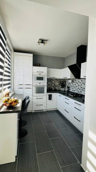 A kitchen in a 3-room apartment with white cabinets, a dark countertop, and fruit decor.