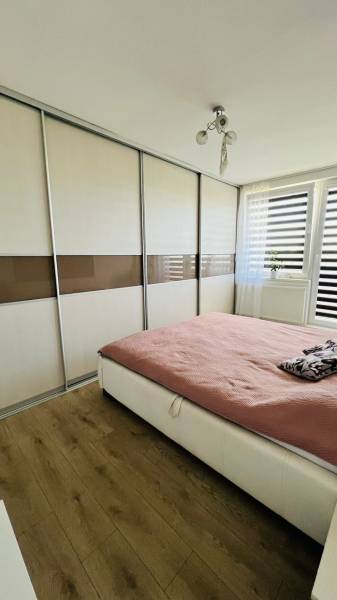 Bedroom with a built-in wardrobe, wood-patterned flooring, and a large window in a 3-room apartment.