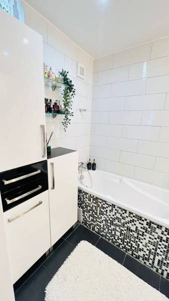 Bathroom in a 3-room apartment with a white bathtub, modern tiles, and storage space.