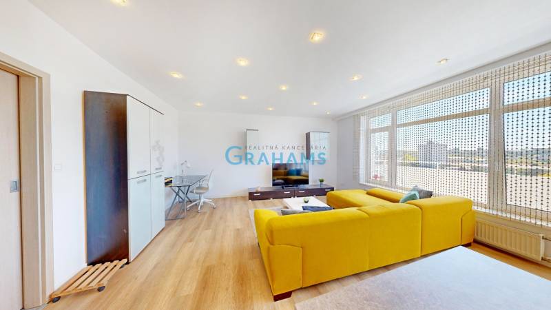 Living room in a two-room apartment with a wooden decor floor and a yellow sofa.
