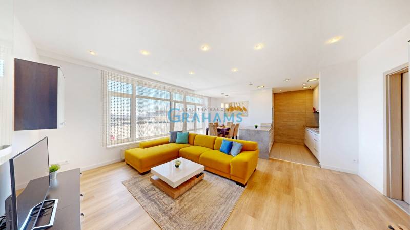 A bright living space with a sofa, dining table, and wood-patterned flooring in a two-room apartment.