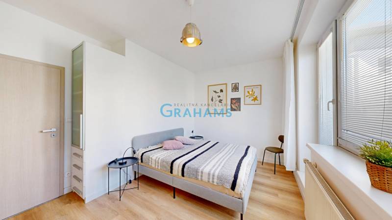 Bedroom in a 2-room apartment with a bed, nightstand, and wooden decor flooring.