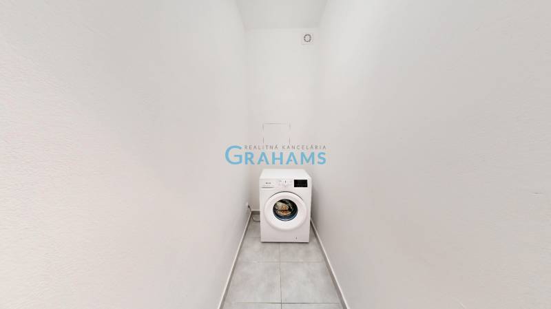 A narrow room with a washing machine in a 2-room apartment, white walls, tiled floor.