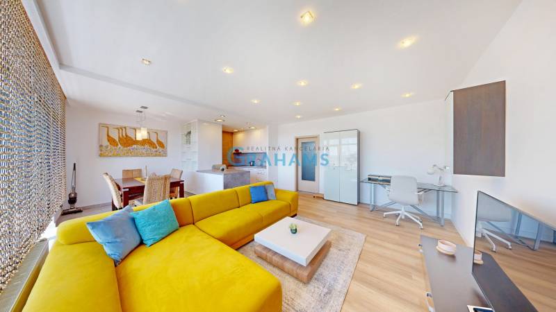 A bright living space with a striking yellow sofa, dining area, and wood-patterned flooring.