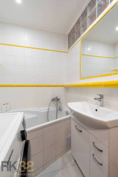Bathroom of a holiday apartment with a bathtub, sink, washing machine, and white tiles.