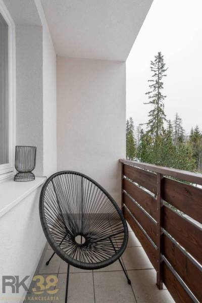 Balcony of a recreational apartment in Poprad with a black chair and a view of the trees.
