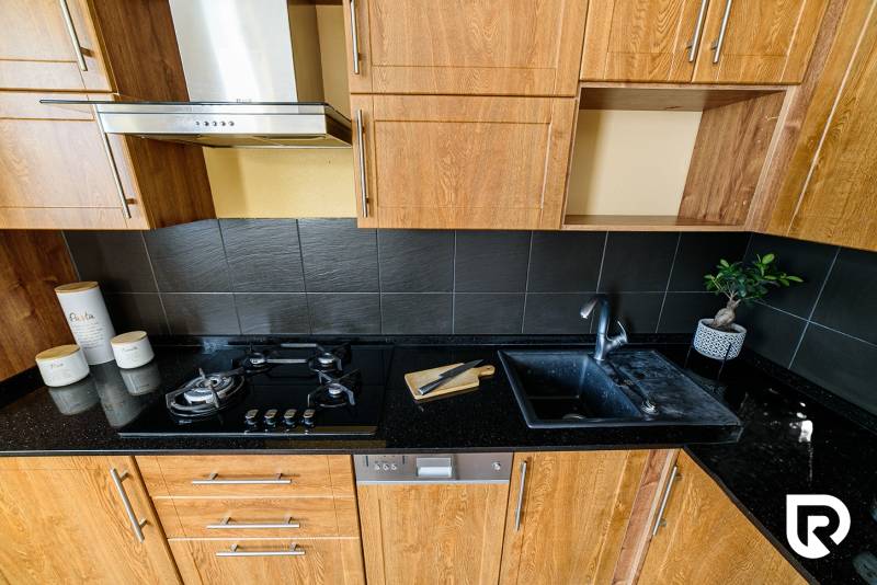 A kitchen unit in a 2-room apartment, with a wooden decor floor and dark tiles.