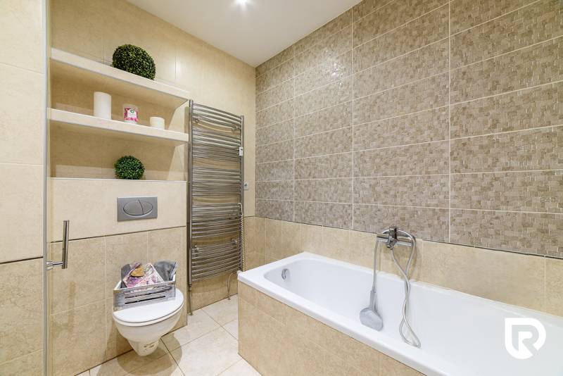 Bathroom with a shower, bathtub, and shelves in a 2-room apartment with neutral tiles.