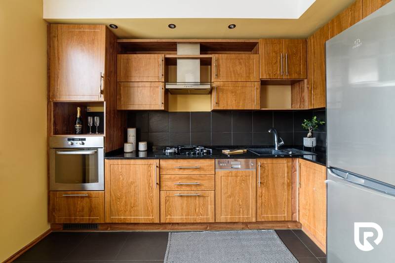 A kitchen in a 2-room apartment with wooden cabinets and a black countertop.