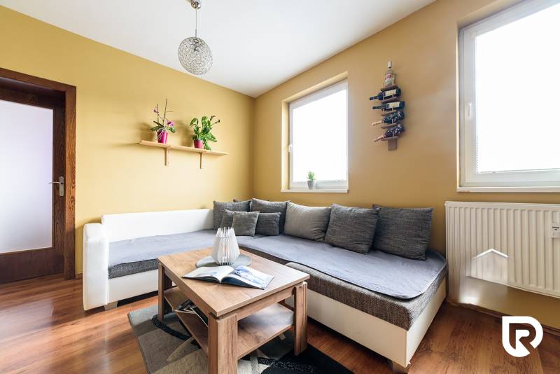 Living room in a two-room apartment with a wood-patterned floor and comfortable seating.