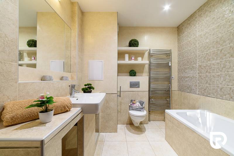 Bathroom in a 2-room apartment with a bathtub, sink, and decorations on the shelves.