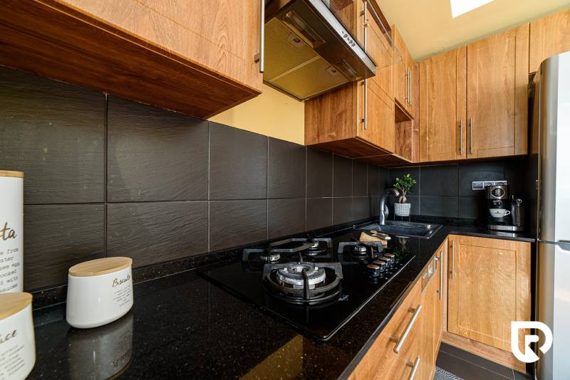 A kitchen with a gas stove, dark tiles, and wooden cabinets in a 2-room apartment.